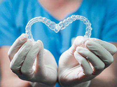 A dental professional s hands holding a heart-shaped transparent dental appliance.